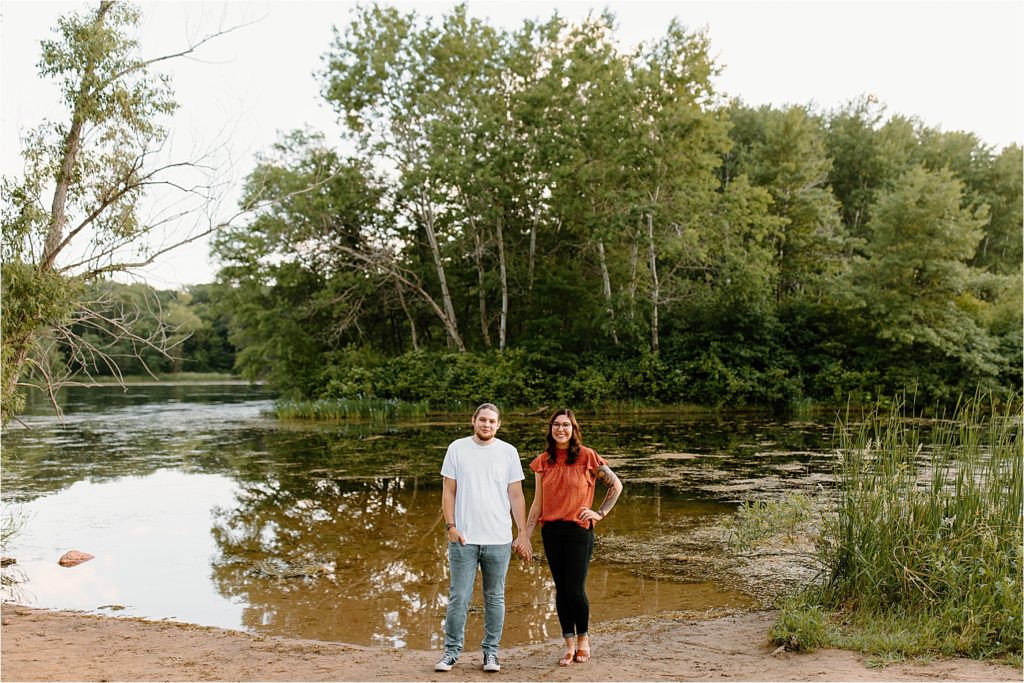 couple holding hands smiling at camera on beach