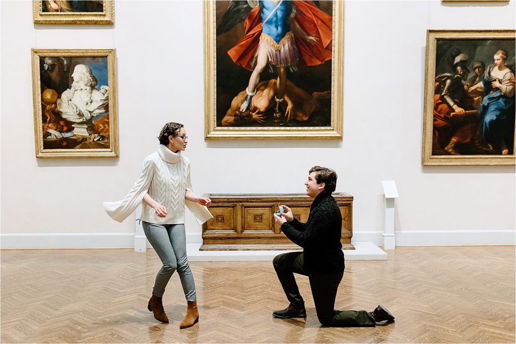 Woman turning around as man on bended knee holding engagement ring at Minneapolis Institute of Art