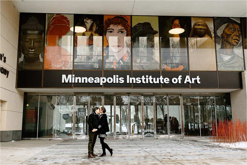 Couple standing in front of entry way doors kissing at Minneapolis Institute of Art in Minneapolis, Minnesota