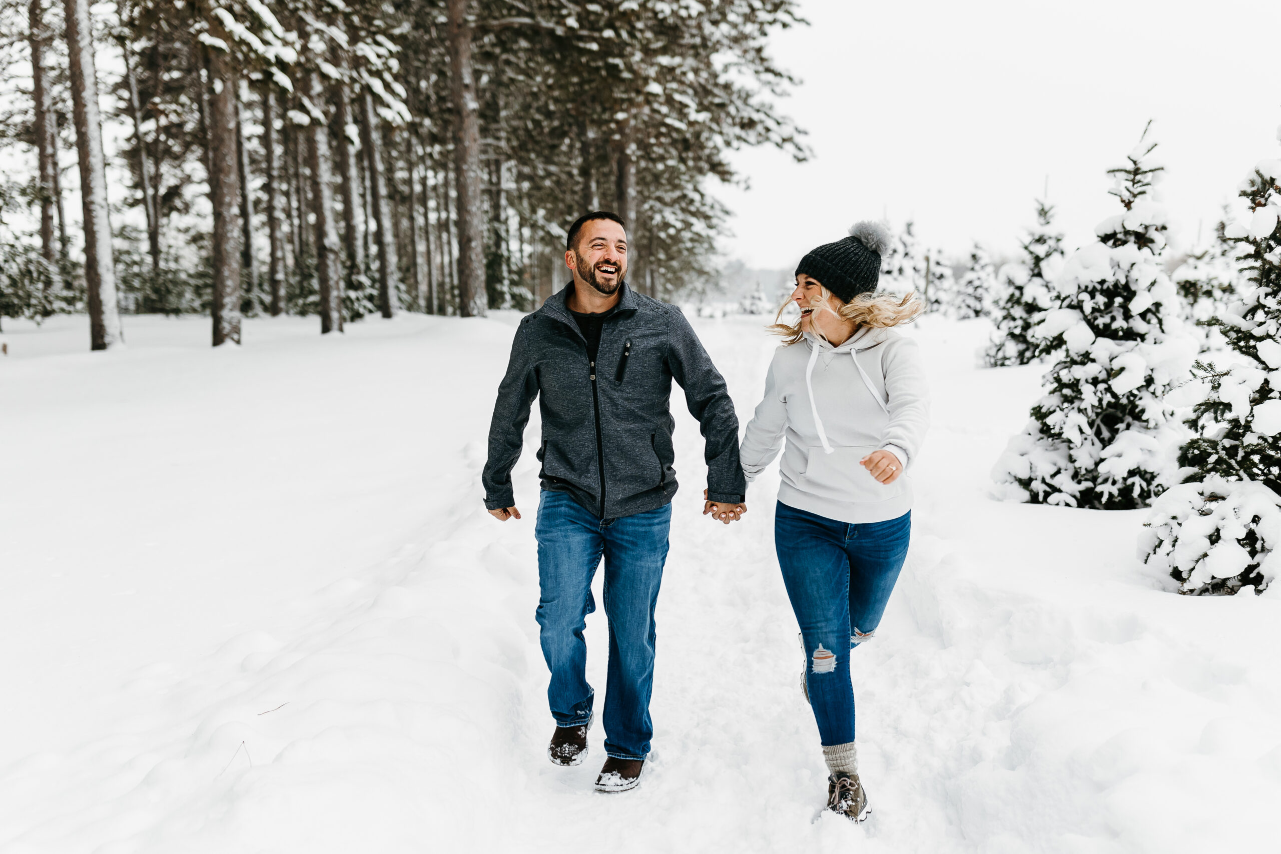 couple holding hands and running in the snow while laughing