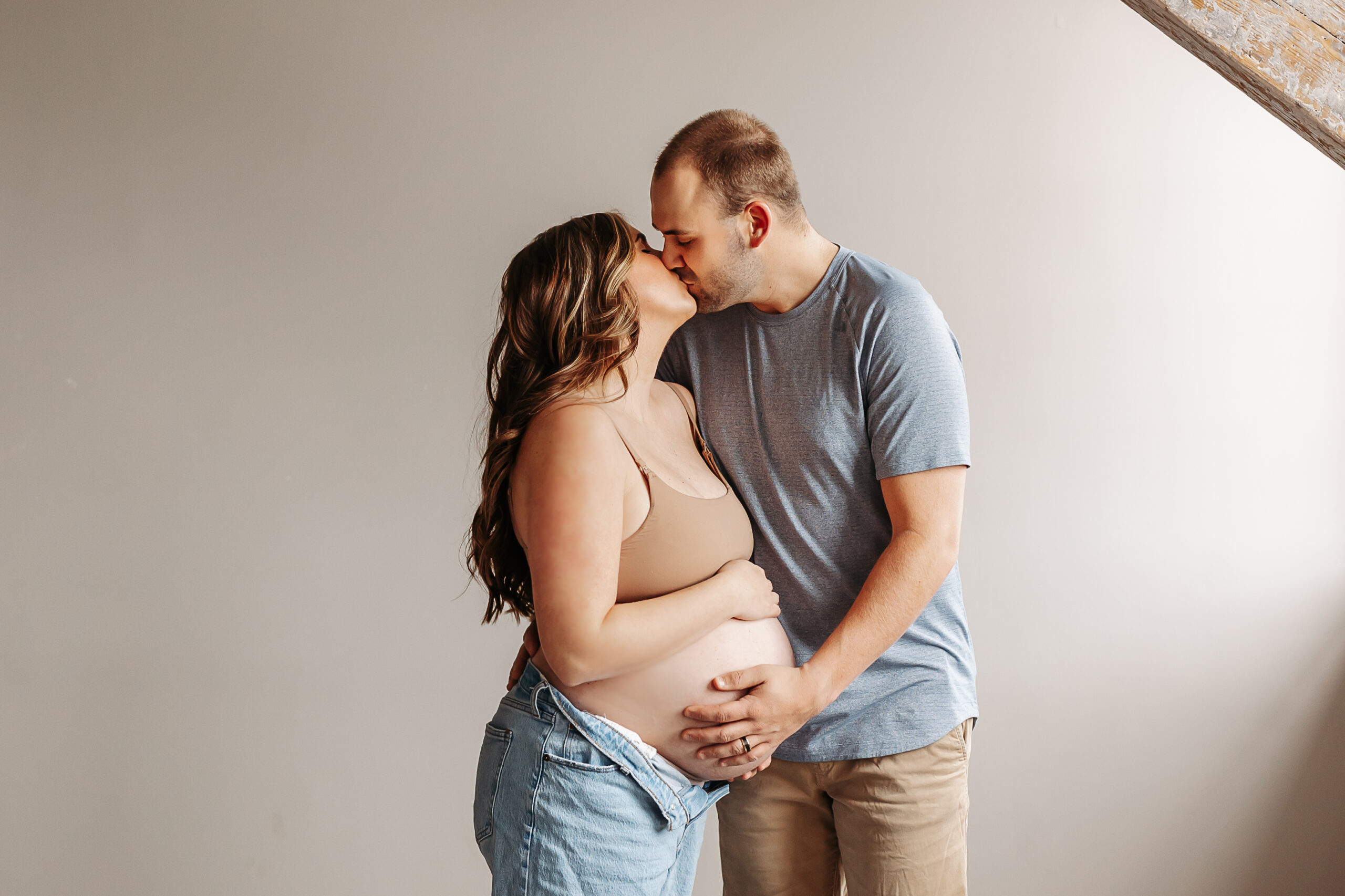 man and woman kissing while both hands are on pregnant belly