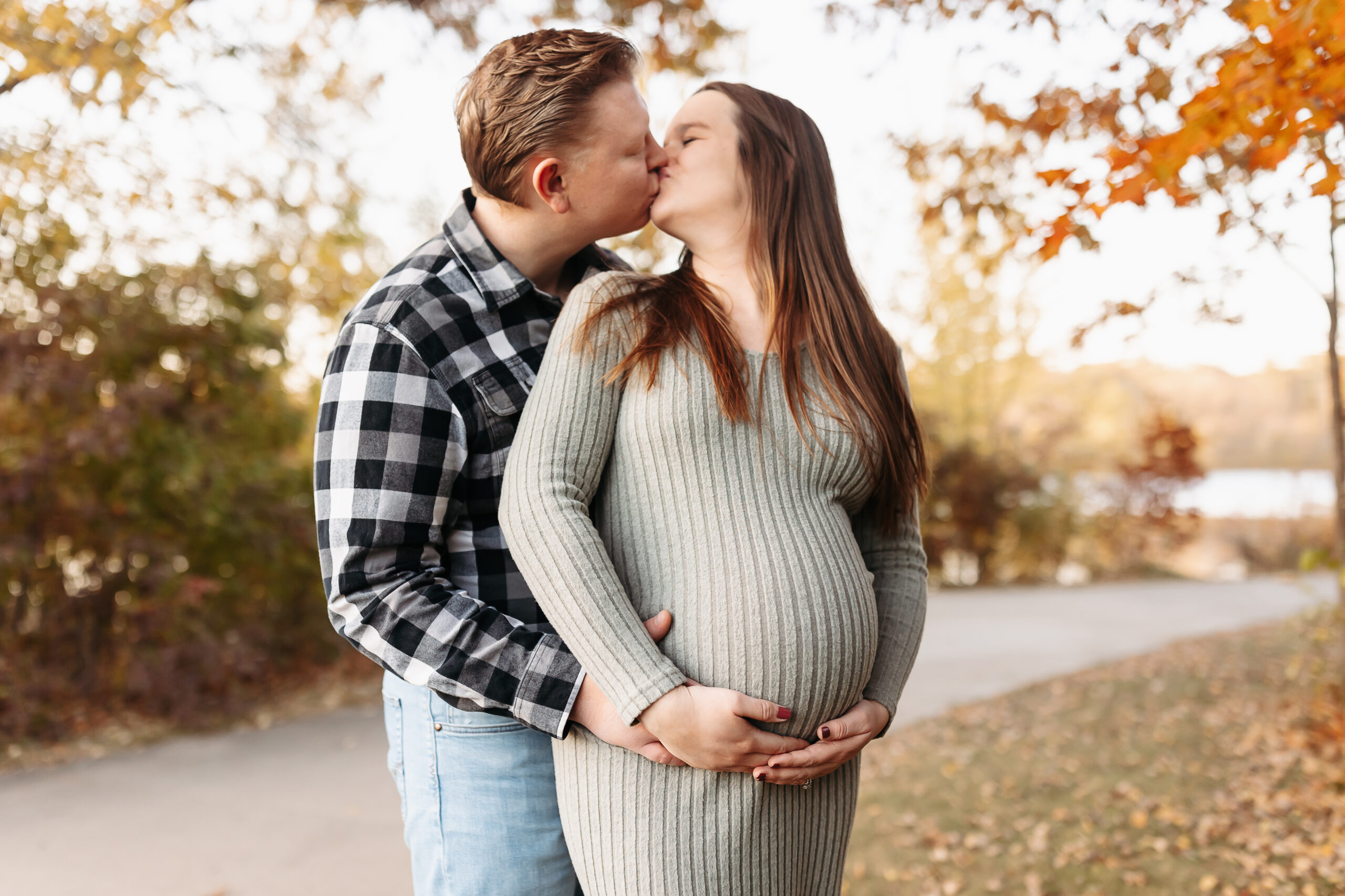 Man standing behind woman kissing with hands on her pregnant stomach.