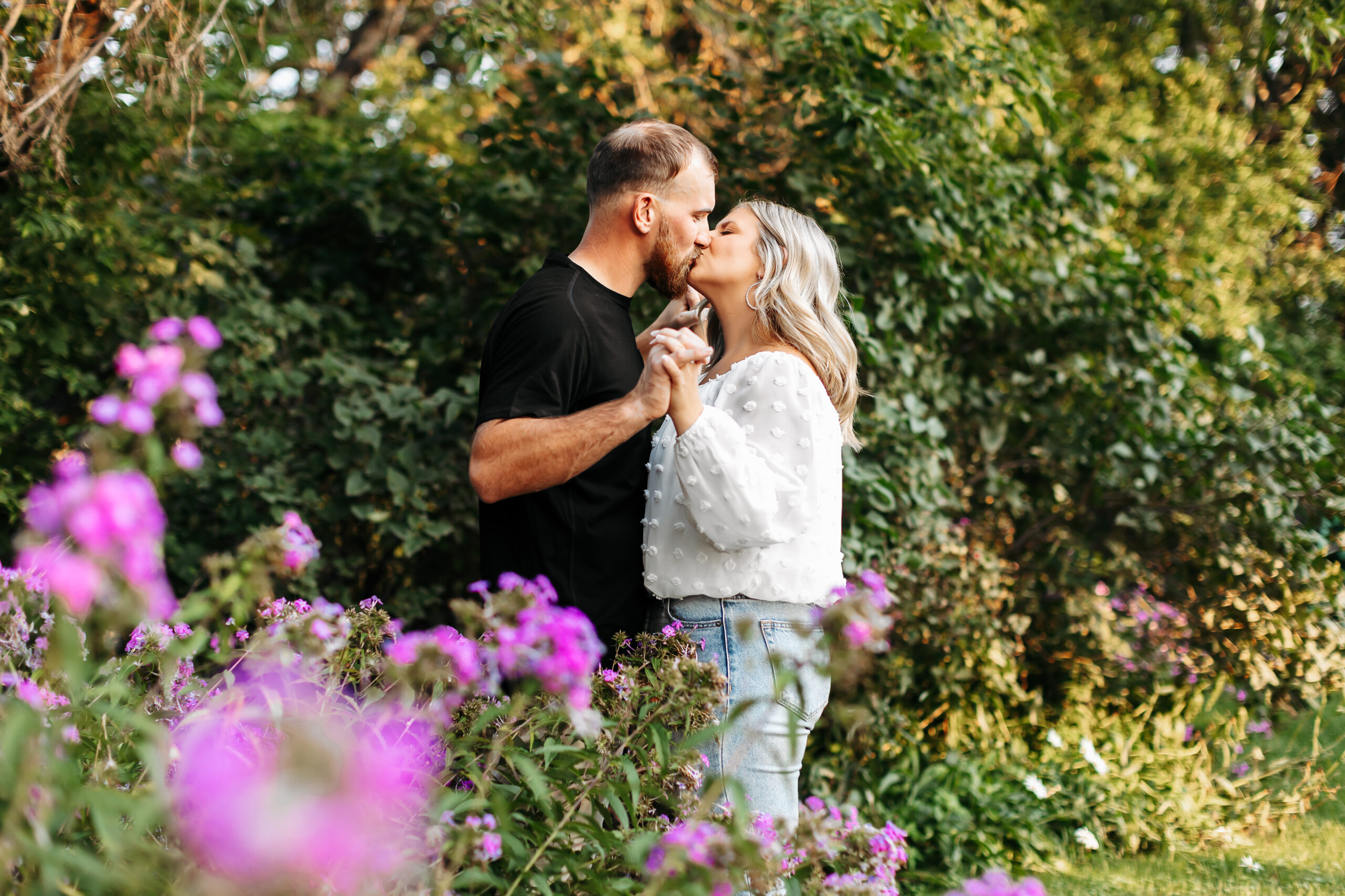 man and woman standing facing eachother kissing while holding hands